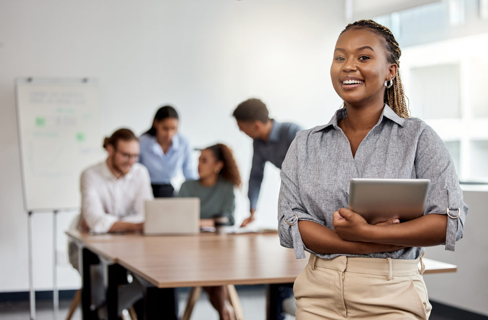MBA student holding an iPad with colleagues behind her.